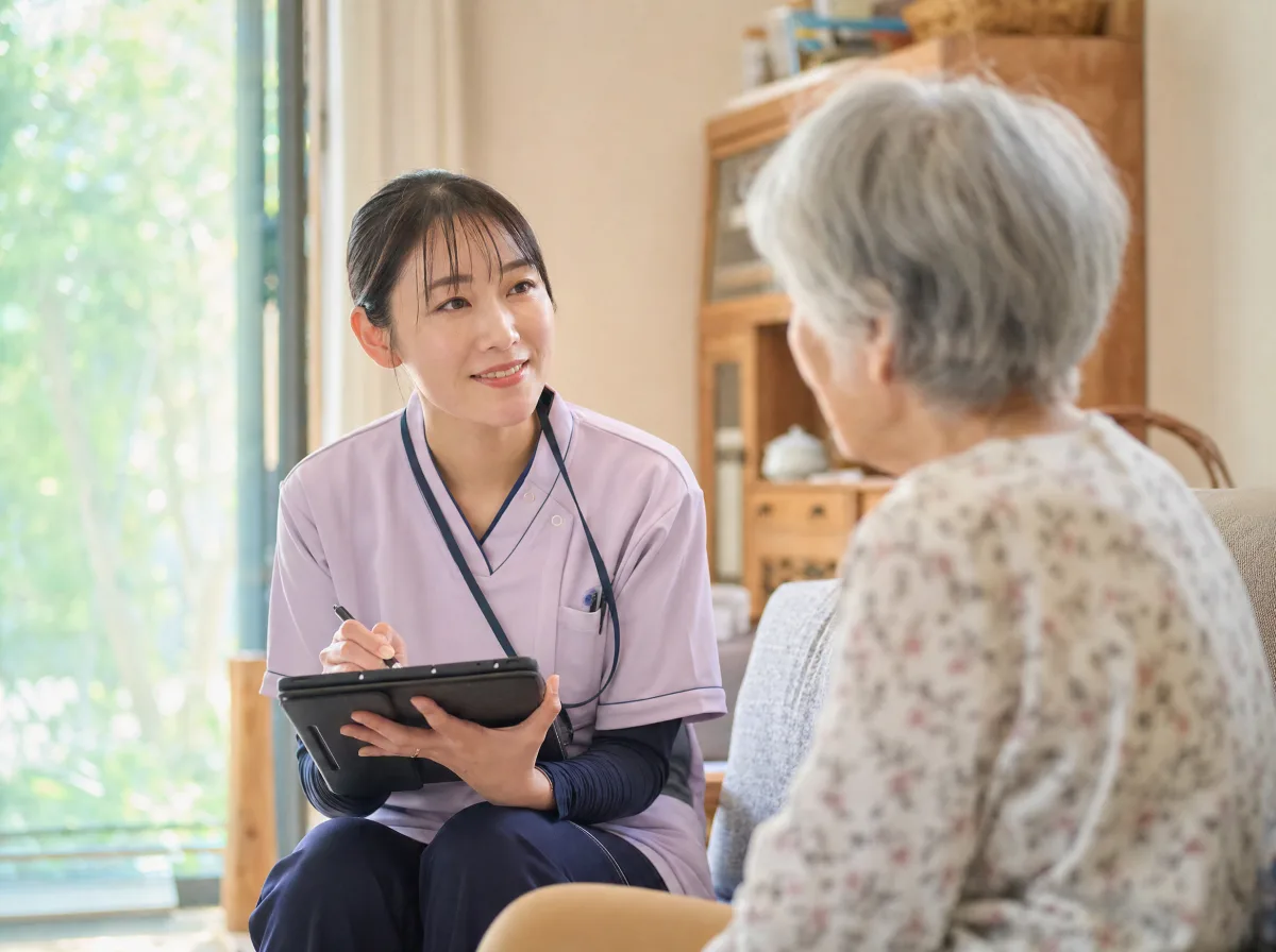 訪問看護師が在宅の患者と話しながらタブレットに記録する様子